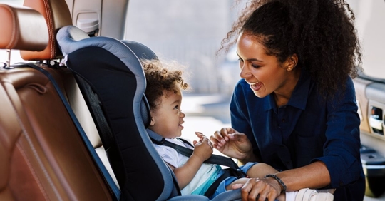 mother buckling her young child into a car seat