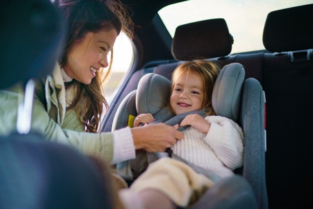 mother fastening little girl in a car seat