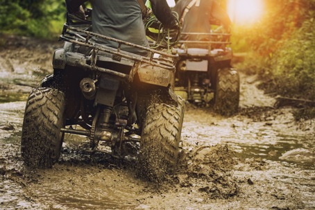 two people riding ATVs off road in the mud